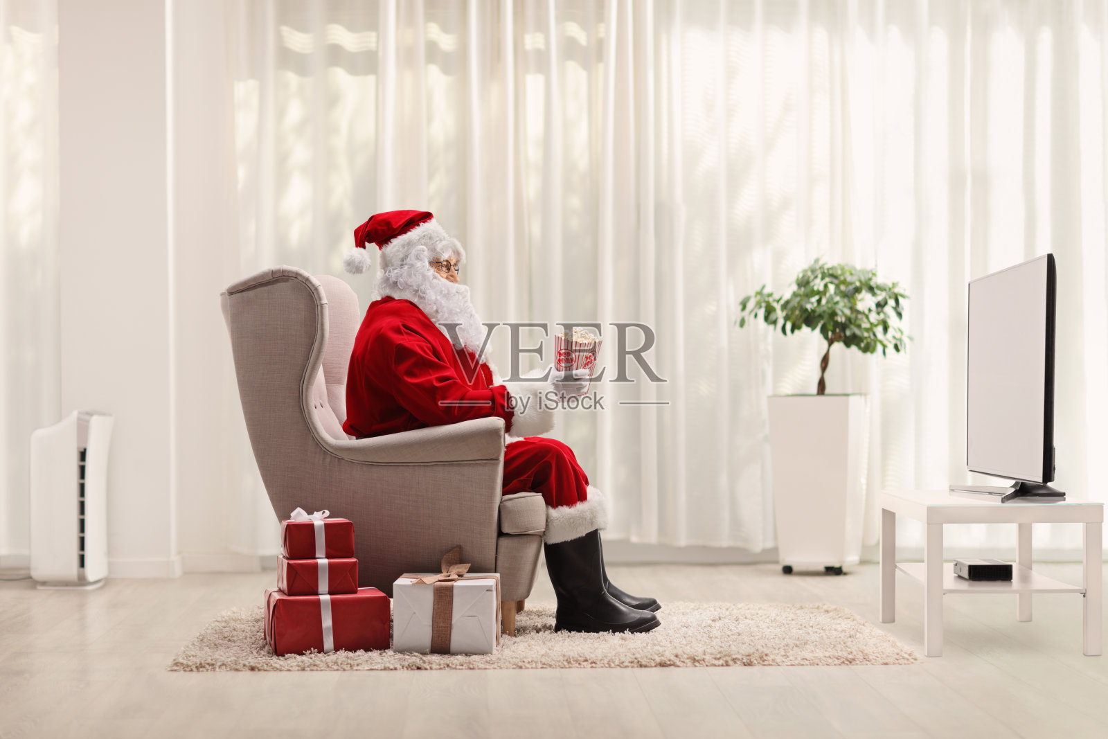 圣诞老人坐在扶手椅上吃着爆米花，在家里看电视照片摄影图片
