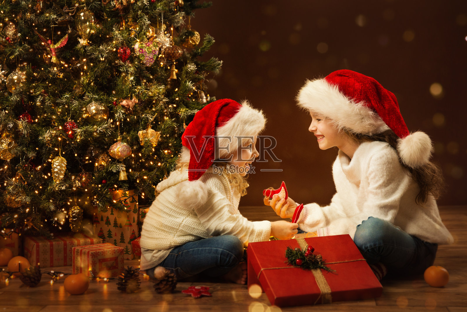 圣诞小女孩打开盒子，给妹妹礼物玩具。快乐的孩子们在圣诞帽下的圣诞树。仙子魔术室内，室内灯光照片摄影图片