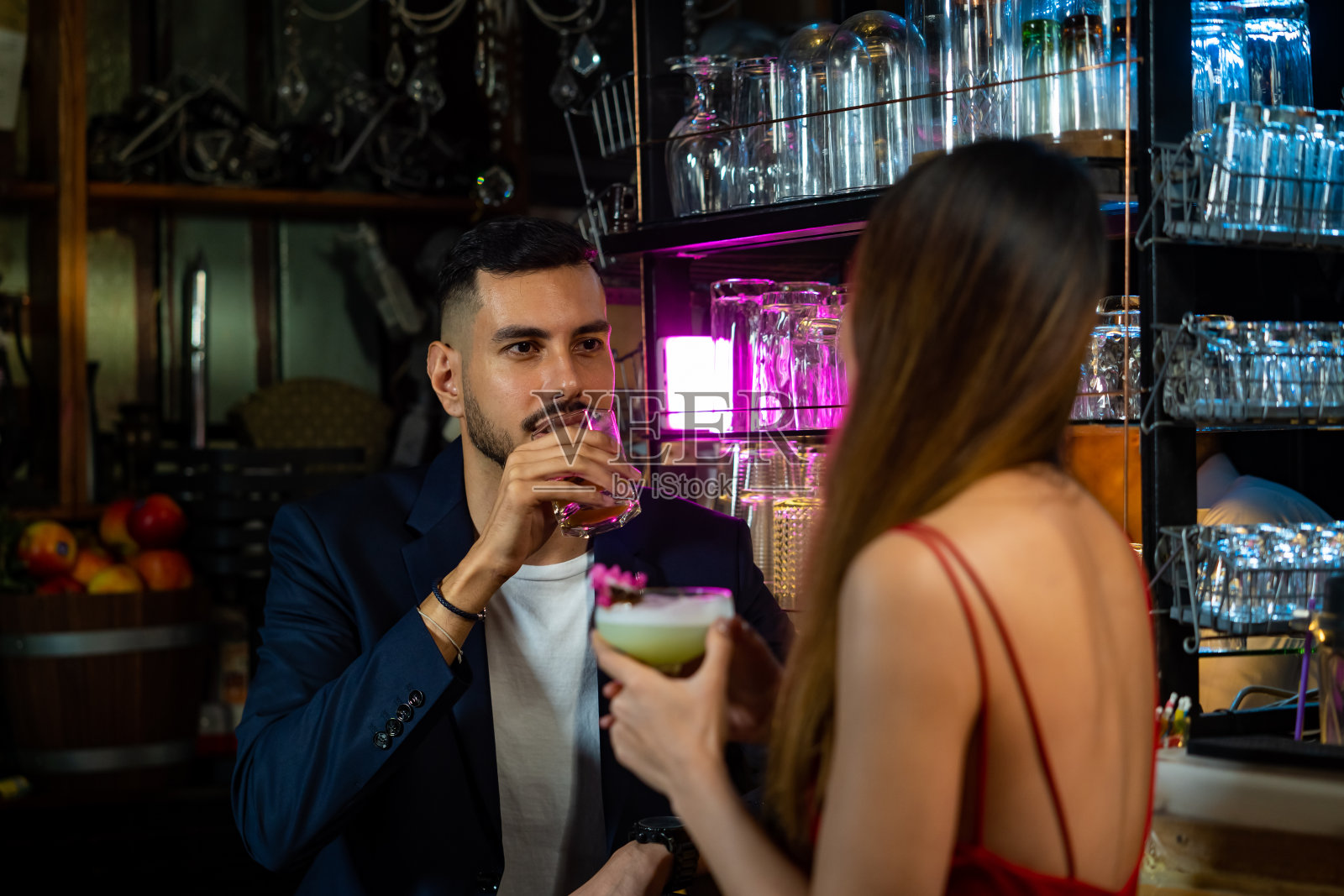 英俊的白人男子站在吧台调情和漂亮的女人在夜总会聚会享受酒精饮料鸡尾酒。微笑的情侣在酒吧享受浪漫的约会。照片摄影图片