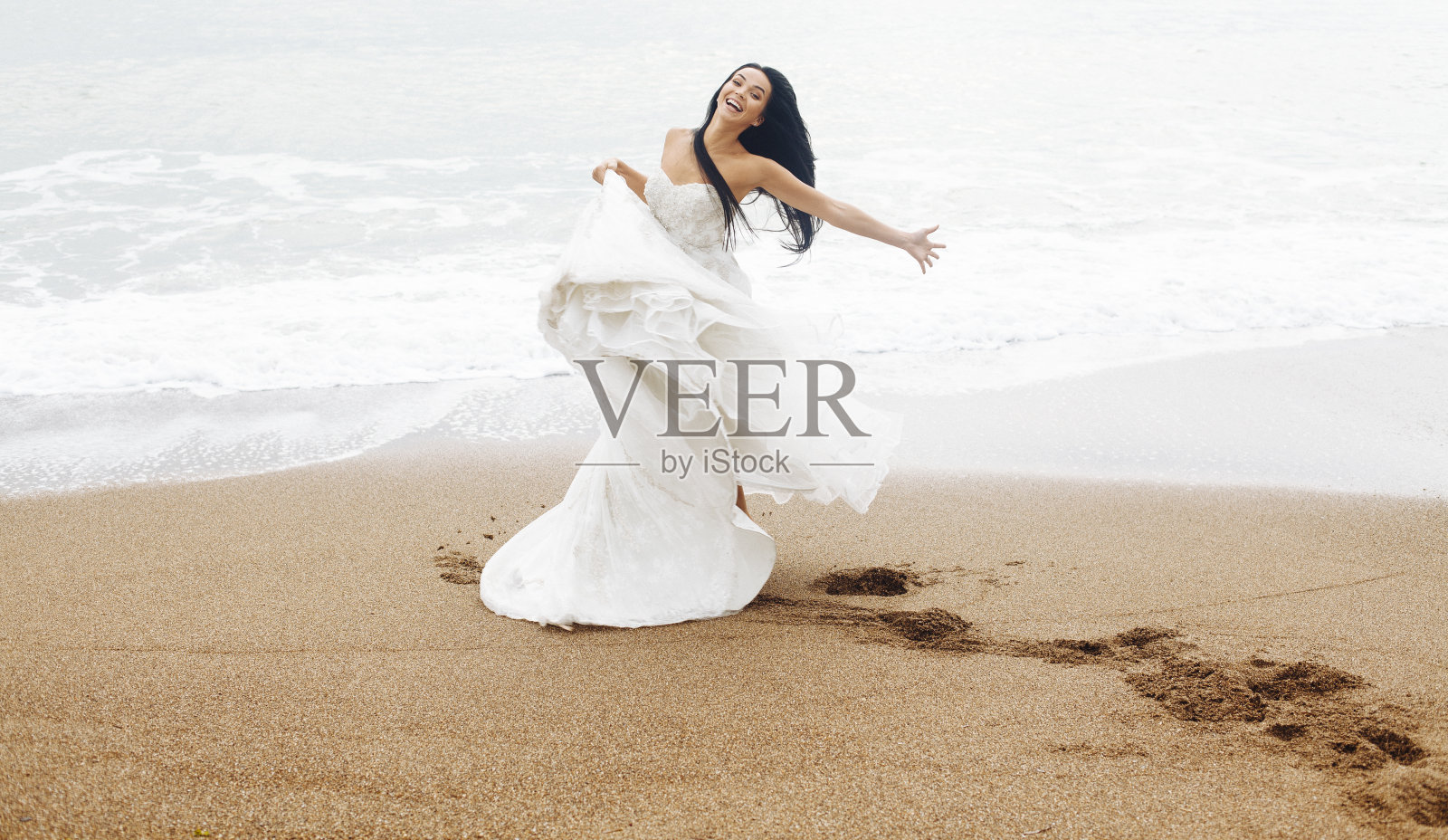 年轻美丽的新娘穿着婚纱在沙滩上跳舞。照片摄影图片