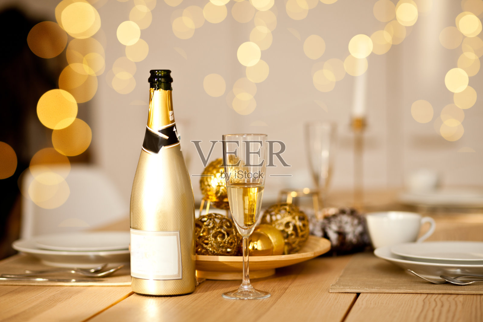 圣诞餐桌设置与节日装饰在一个金色。新年的庆祝活动。一瓶和一杯香槟。照片摄影图片