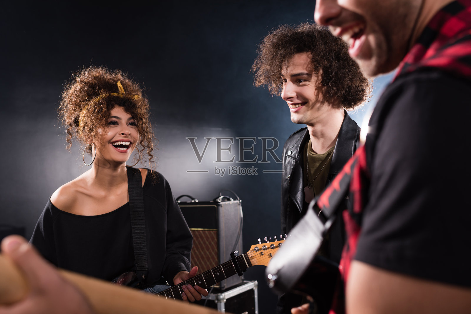 微笑的音乐家站在靠近卷卷的女人低音吉他模糊吉他手在前景照片摄影图片