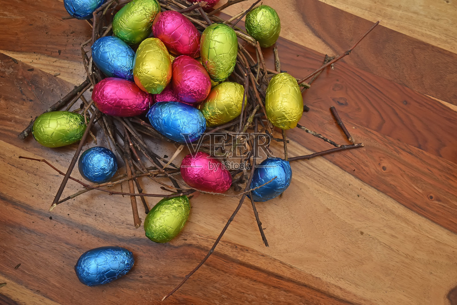 用锡箔纸包好五彩缤纷的复活节彩蛋，用树枝和小树枝搭成一个天然的巢，以棕色的木质为背景，点缀着粉色、绿色、蓝色和黄色。照片摄影图片