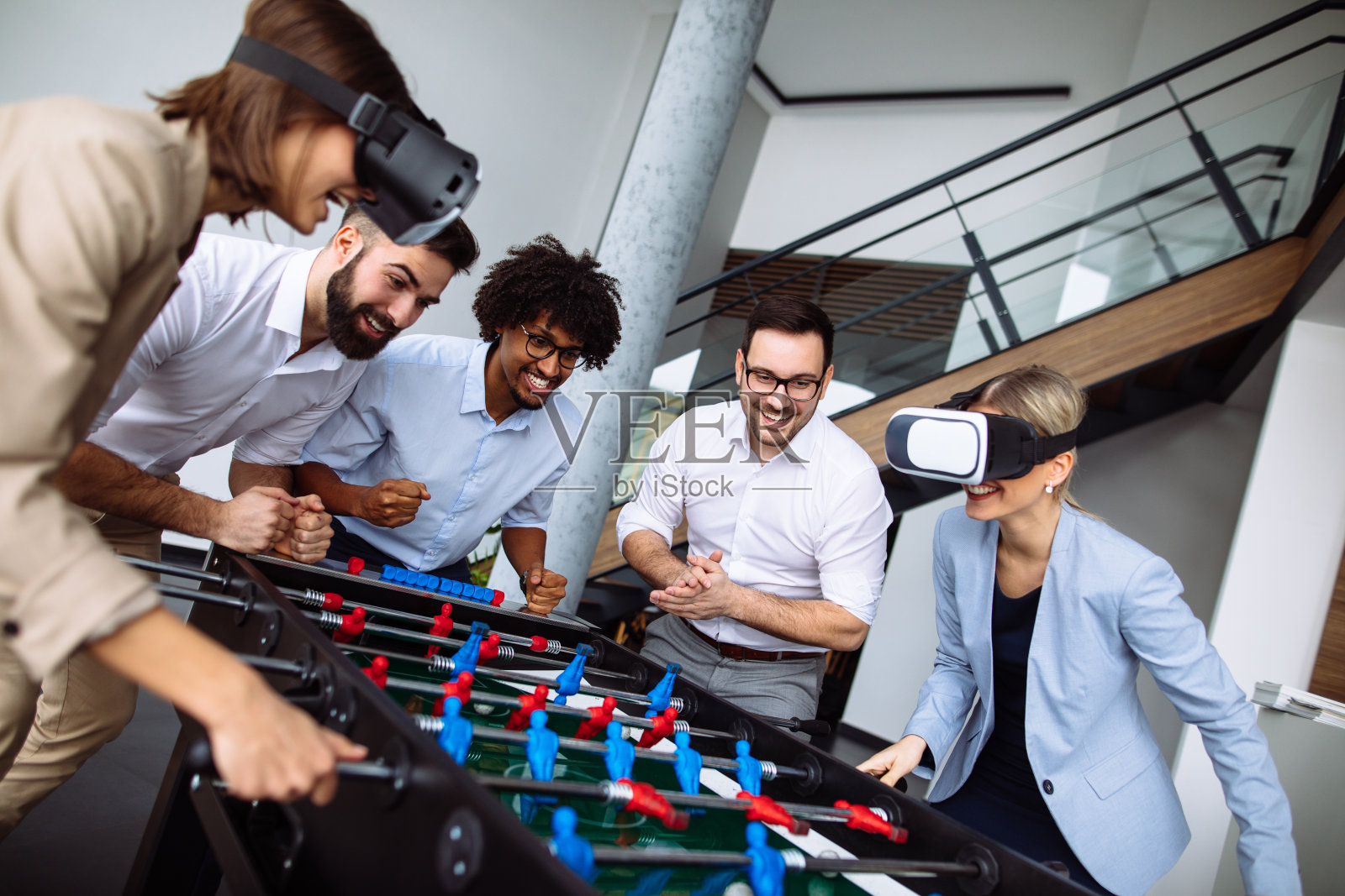 年轻的办公室职员用虚拟现实头盔玩桌上足球照片摄影图片