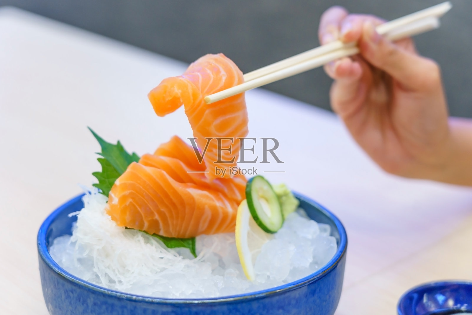 用筷子夹着鲑鱼生鱼片-新鲜的生鲑鱼切片加芥末冰，日式料理。照片摄影图片