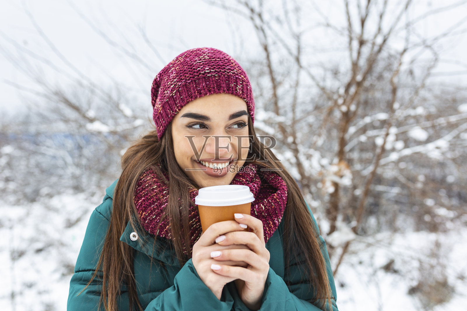 快乐的年轻女子与一次性杯咖啡或茶穿暖和的衣服。美丽的女孩拿着一次性杯子，站在室外的冬天照片摄影图片