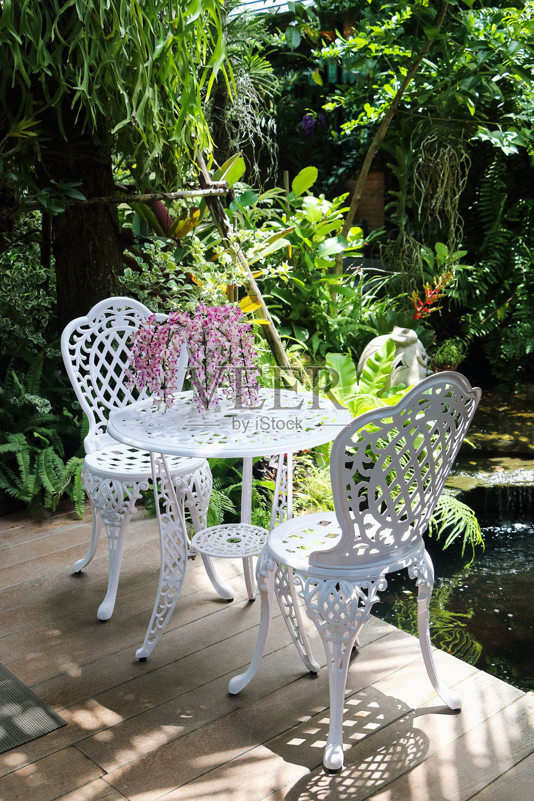 一套白色桌椅，饰以兰花花瓶，园中有池塘照片摄影图片