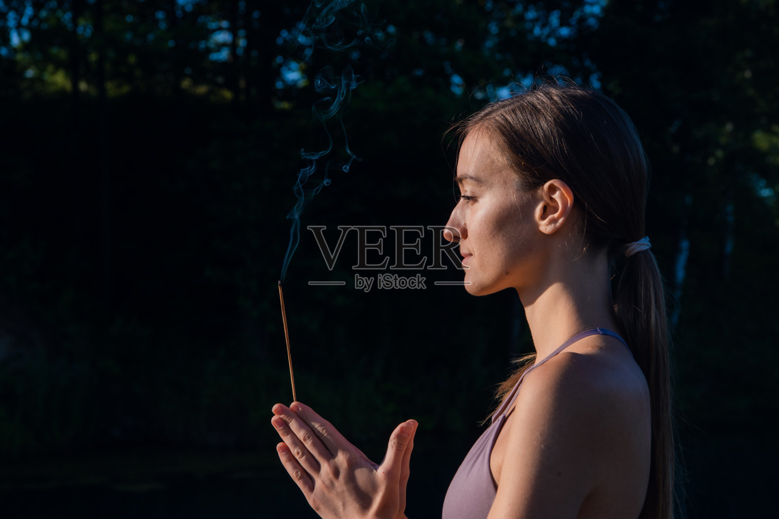 一个女人在户外做瑜伽冥想，手里拿着香薰棒，手掌合十礼照片摄影图片