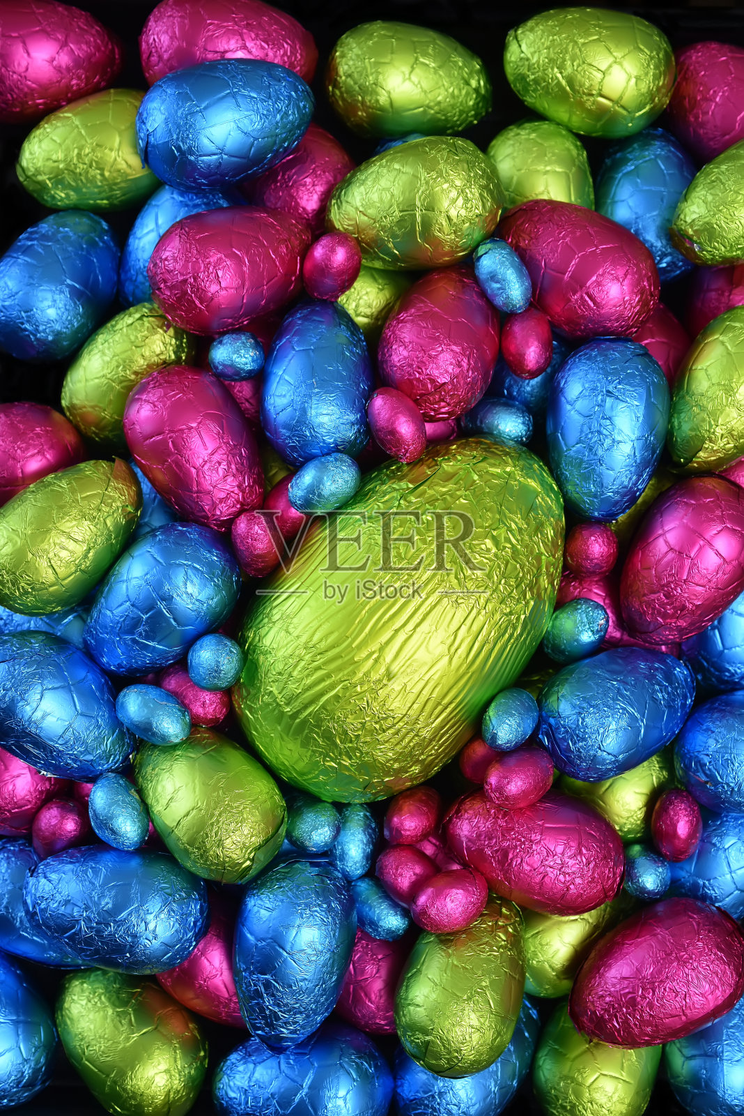 1 .用锡箔纸包裹一堆或一组颜色各异、大小各异的巧克力复活节彩蛋，彩蛋的颜色有粉色、蓝色、黄色和酸橙绿，中间放一个绿色的大鸡蛋。照片摄影图片
