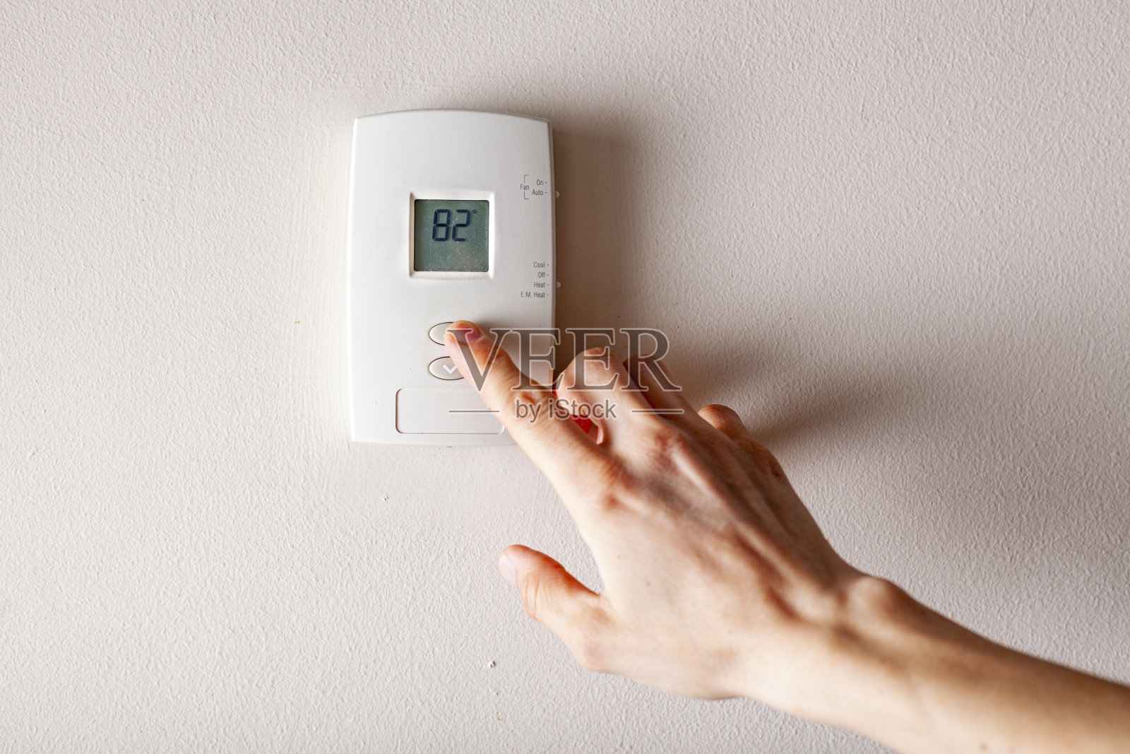 一名妇女正在按墙上装有数字显示温度的恒温器的向上按钮照片摄影图片