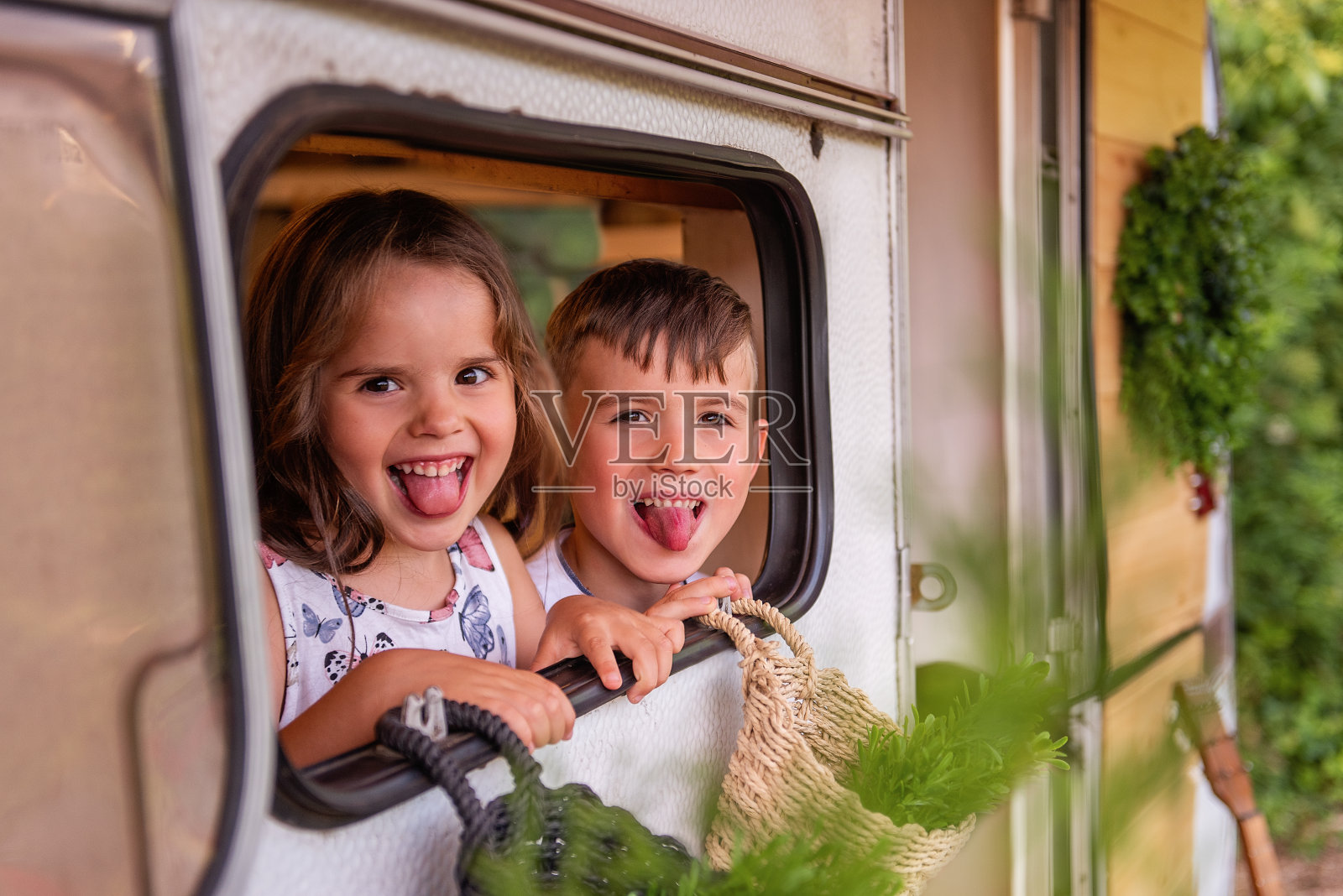 快乐的孩子们看着他们的拖车窗外。弟弟和妹妹和他们的父母在露营中休息。欢乐的一家人在城外野餐。美丽的女孩和男孩笑，微笑照片摄影图片