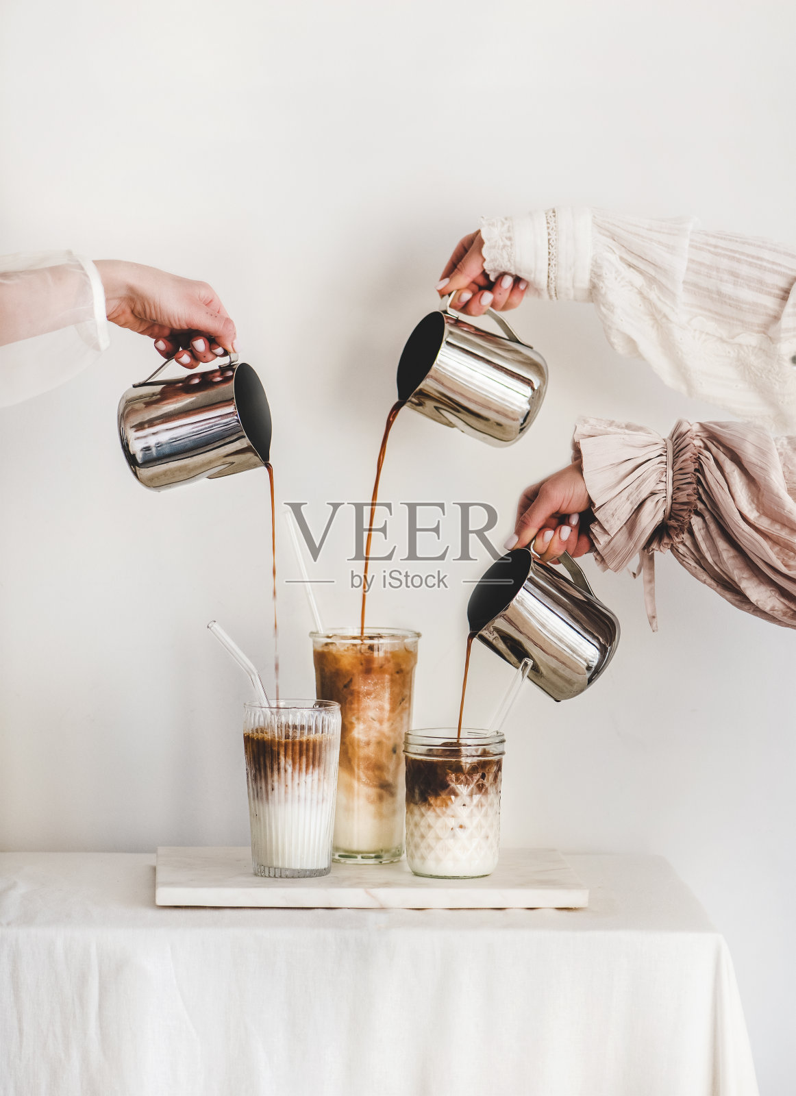 女性用双手将咖啡倒进玻璃杯，加入牛奶，制作拿铁咖啡照片摄影图片