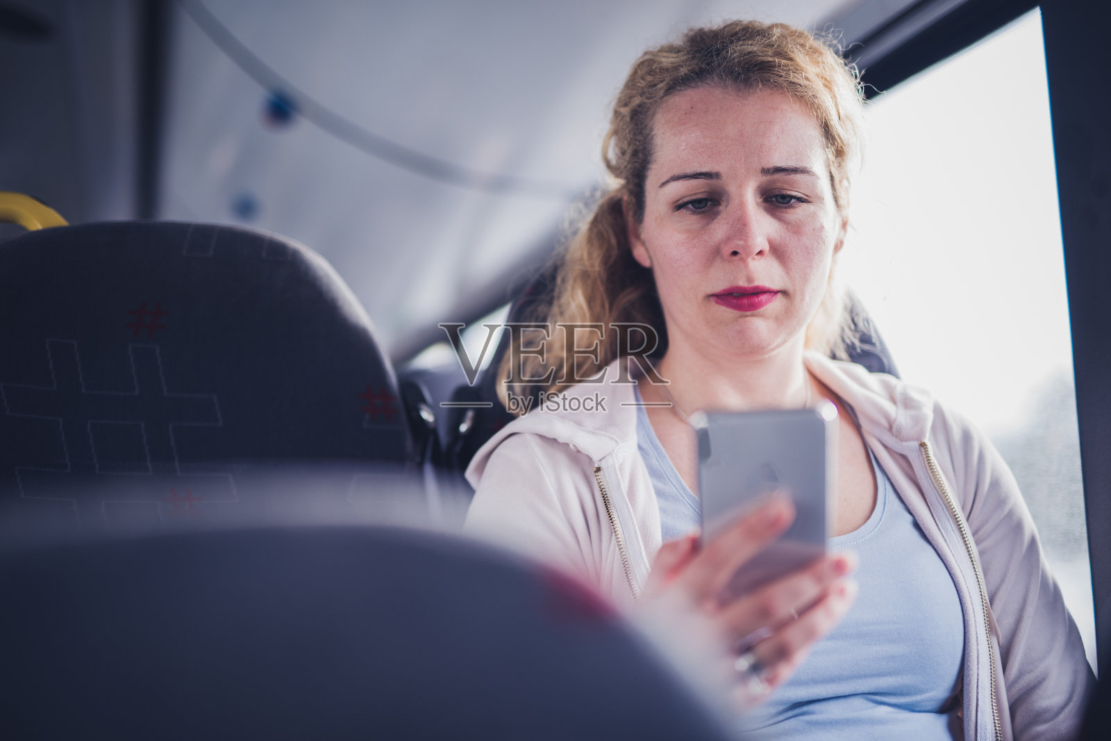年轻漂亮的女人在公共汽车上使用手机。照片摄影图片