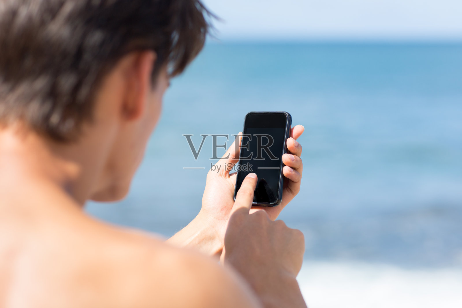 一名男子在海滩上使用触屏手机。照片摄影图片