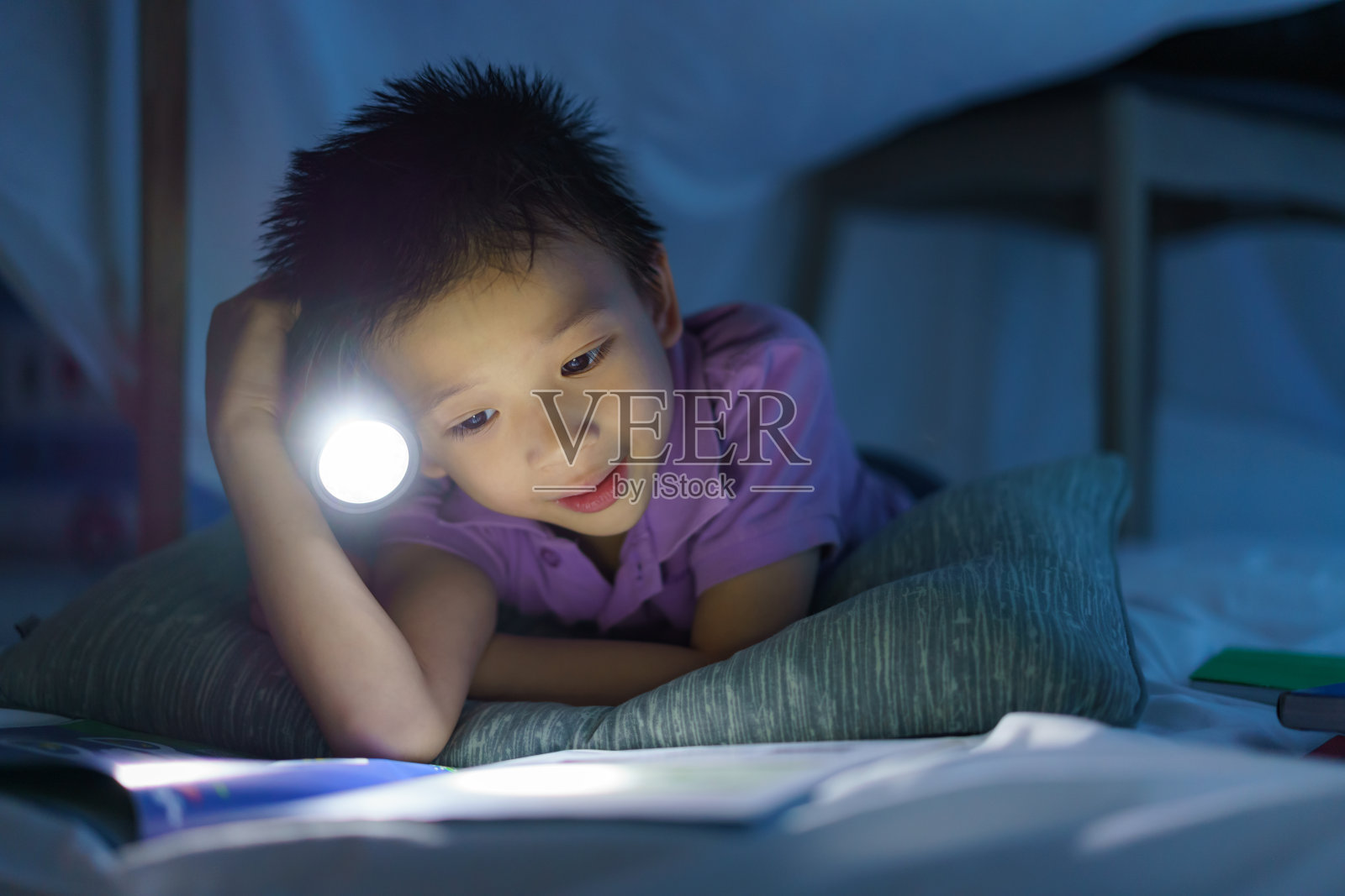 亚洲学前班的小男孩在家里的客厅里用手电进行想象游戏和读书。照片摄影图片