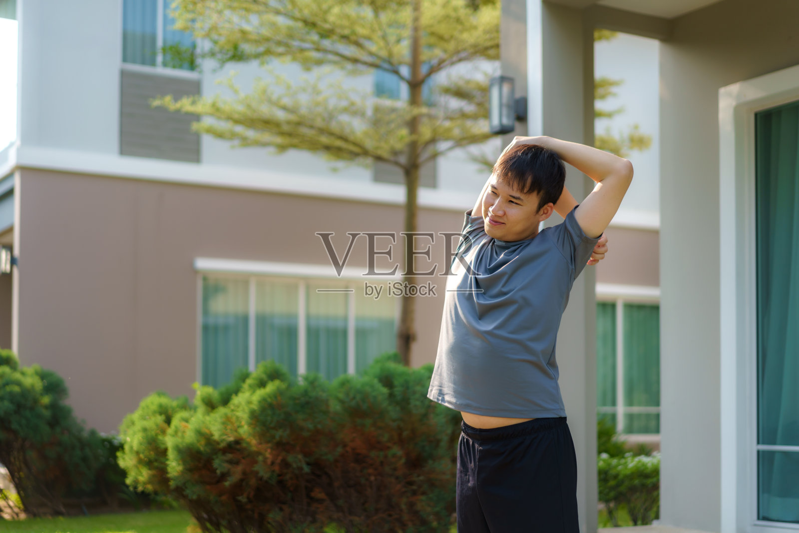 亚洲男人伸展运动前或运动后，在邻居家的前门附近，为身体和精神上的健康和幸福做热身或降温运动。照片摄影图片