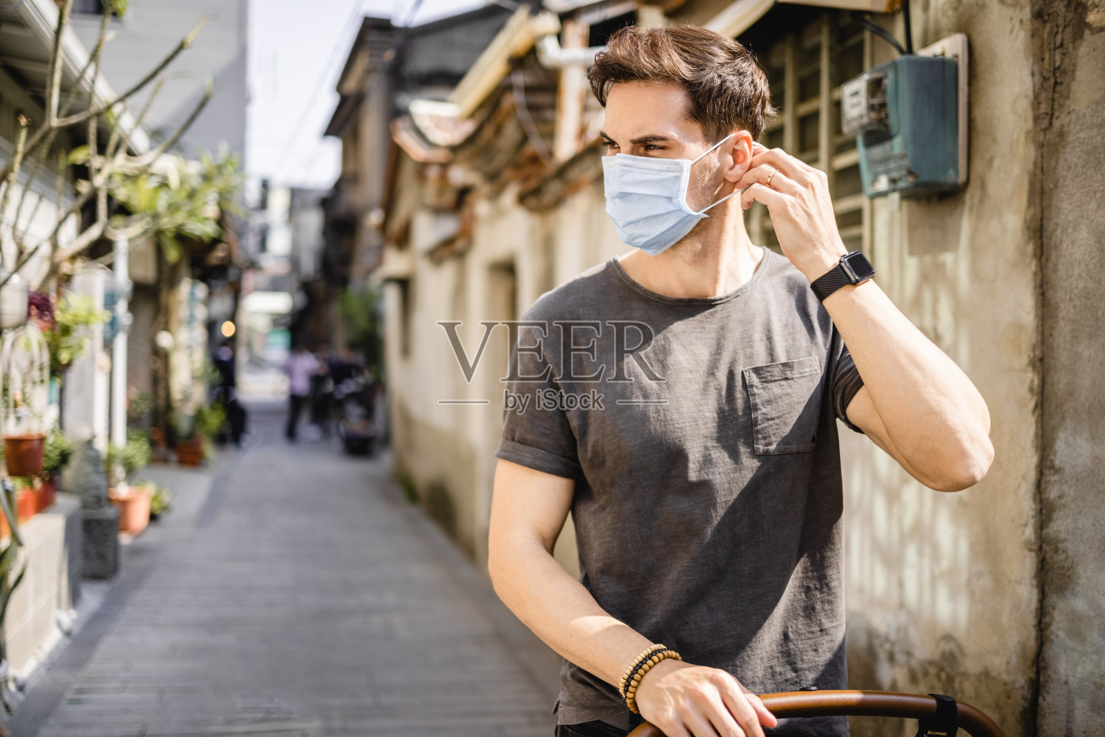 一个戴着外科口罩的英俊男子在小老街照片摄影图片