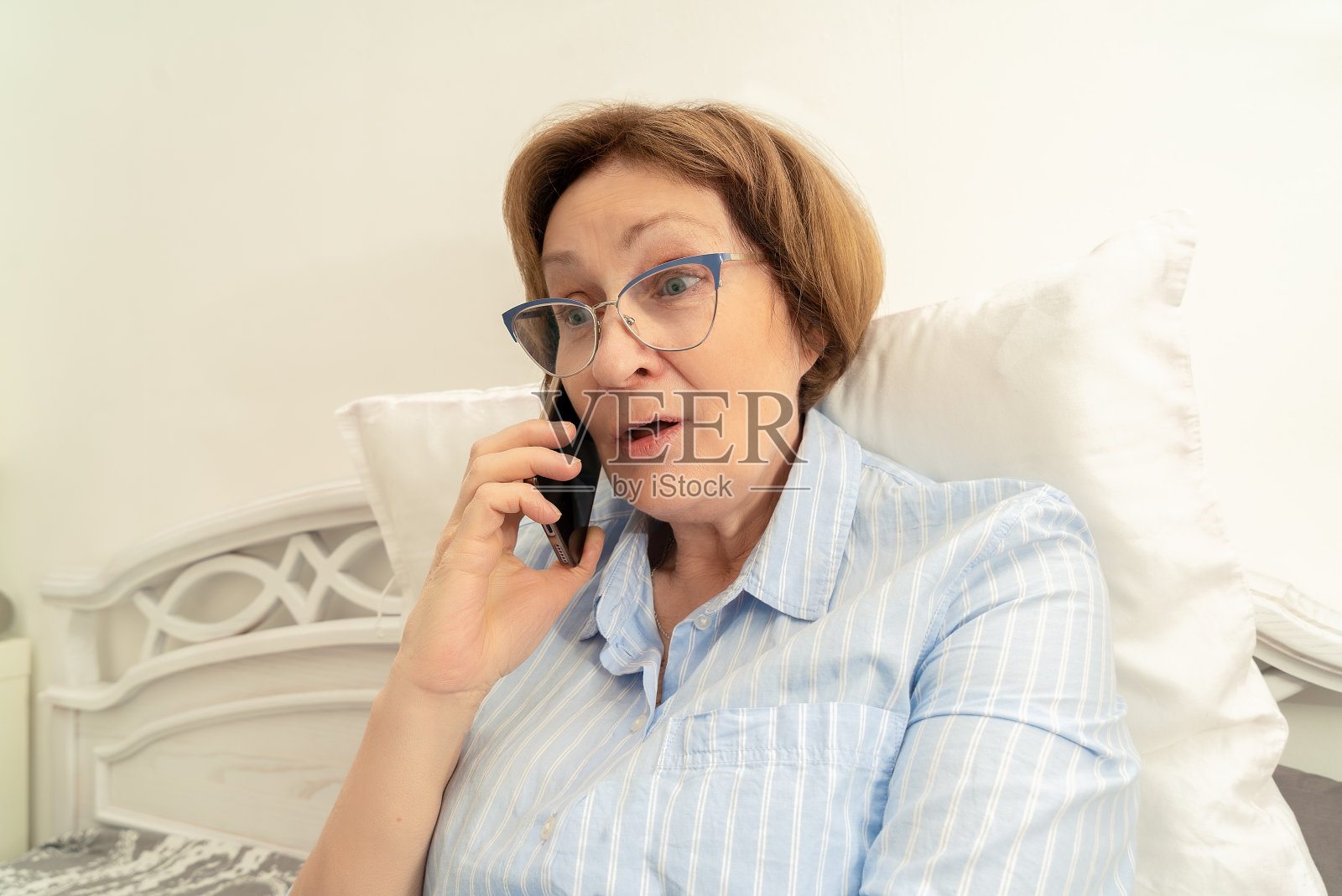 戴眼镜的老年妇女用手机说话，表示惊讶照片摄影图片