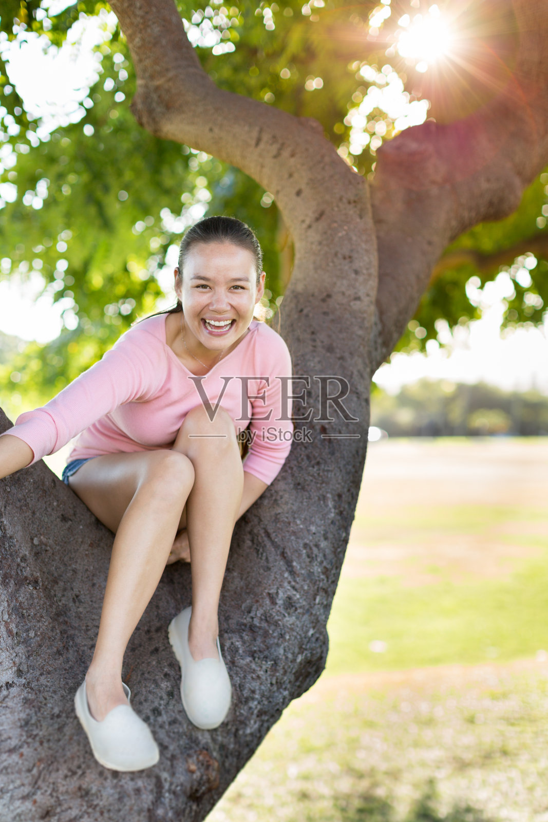 快乐快乐的女人坐在公园的一棵树上玩。照片摄影图片