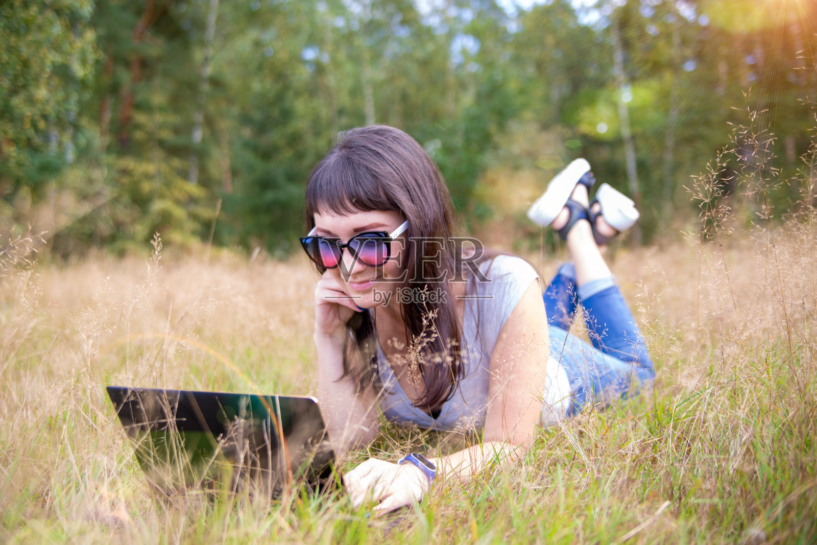 一个快乐的年轻女人，在阳光明媚的草坪上拿着笔记本电脑。自由职业者在大自然中工作。远程学生学习照片摄影图片
