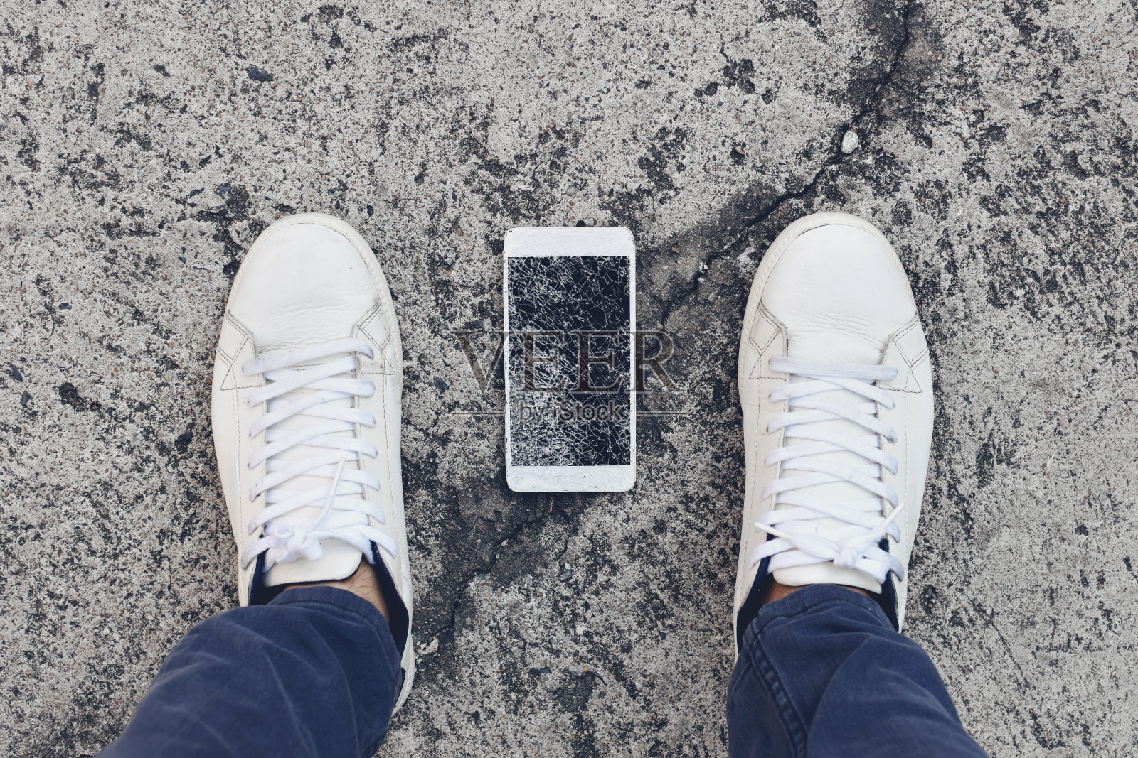 一只智能手机掉在地上，正好被主人的鞋子夹在中间。照片摄影图片