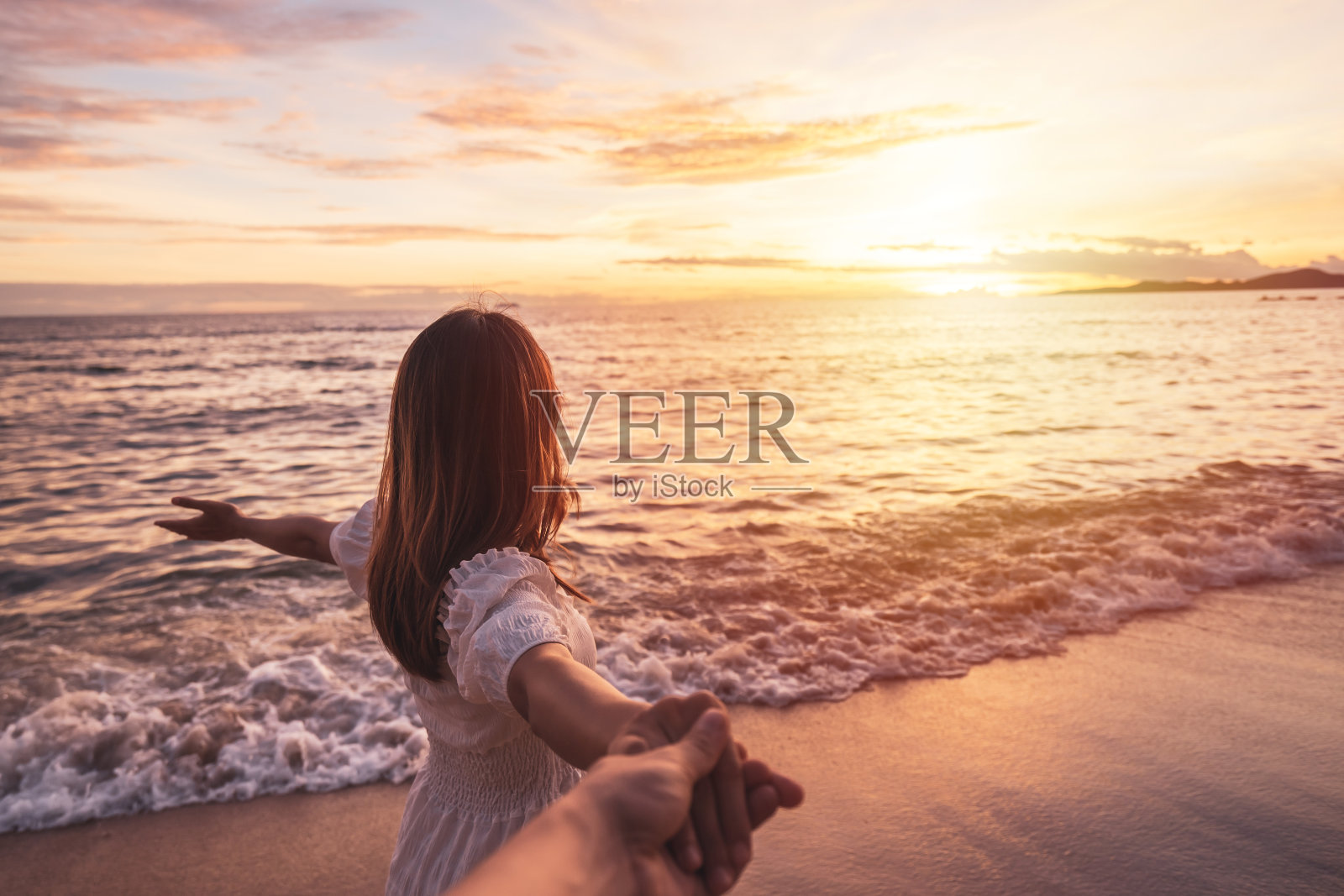 年轻的女人旅行者牵着男人的手，在海滩上看美丽的日落，夫妇在夏天的概念度假照片摄影图片