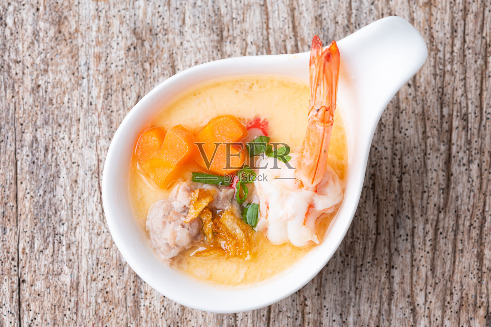 木桌上的瓷碗里放着自制的虾和蔬菜蒸蛋。健康食品的概念。照片摄影图片