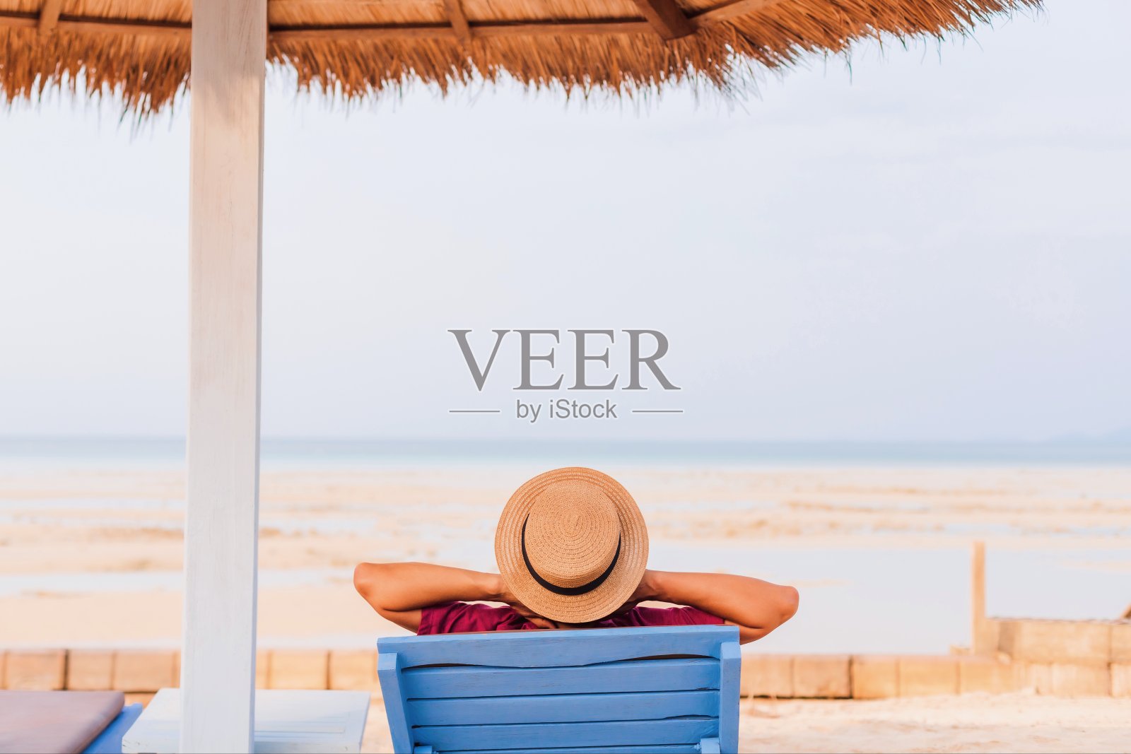 在夏日的海边，一个游客正躺在沙滩椅上，背景是蓝色的天空。周末快乐旅行的概念。照片摄影图片