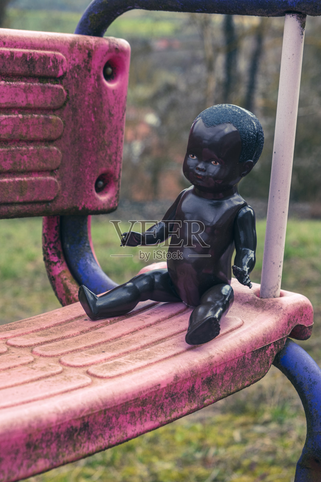 黑色娃娃坐在废弃的游乐场的秋千上的特写照片摄影图片