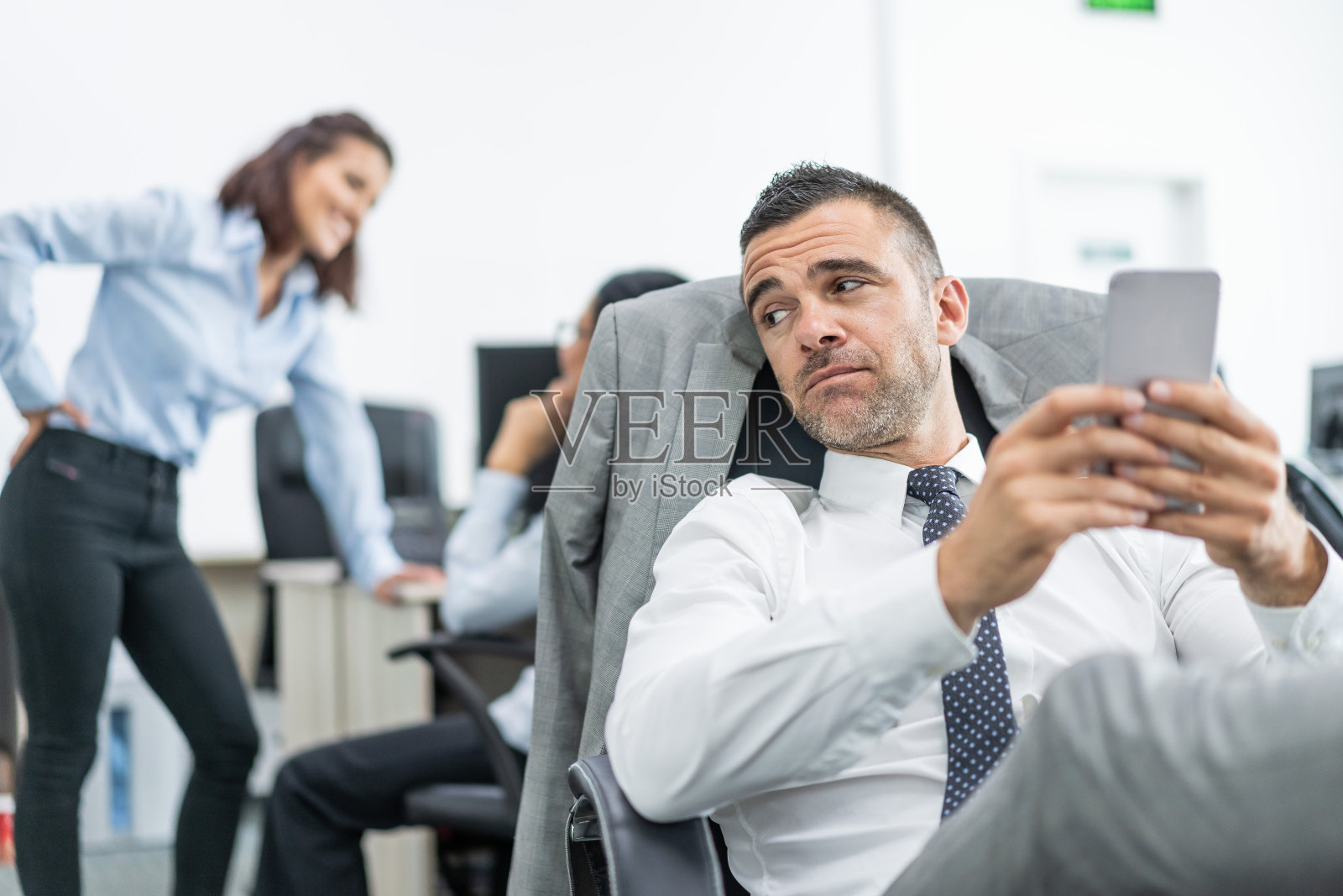 成功的经理坐在办公室中间，看着他的手机照片摄影图片