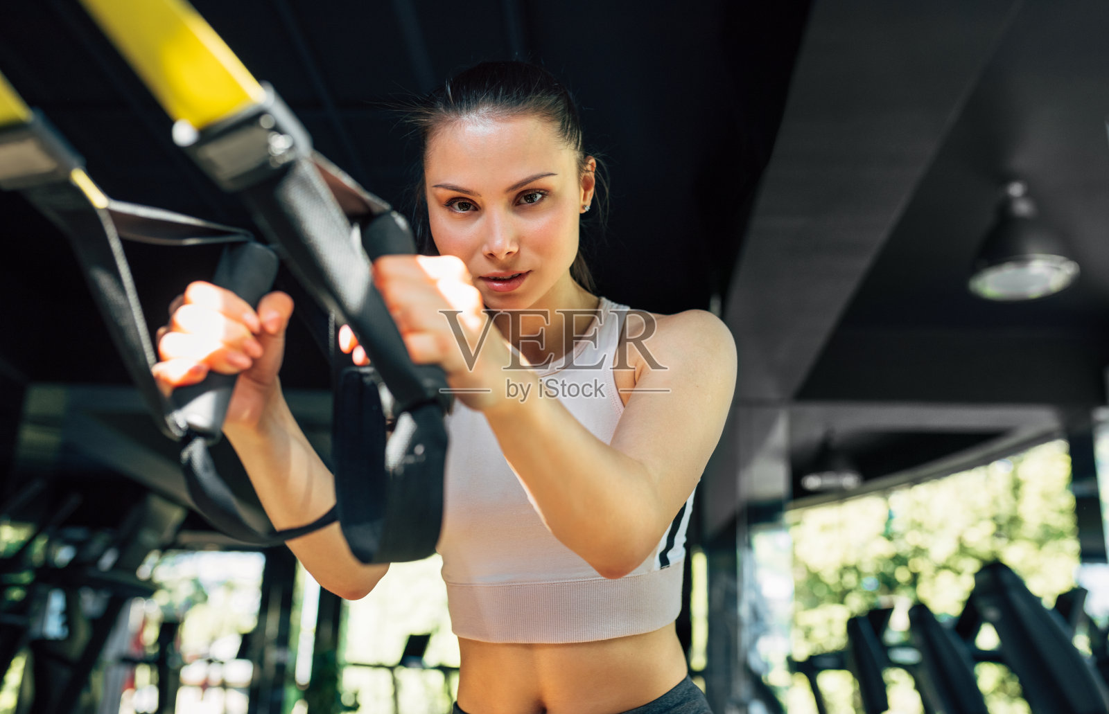 年轻女子在运动服装训练与健身trx肩带在健身房。运动员女性与健康的身体锻炼她的肌肉悬吊肩带在健身房。照片摄影图片