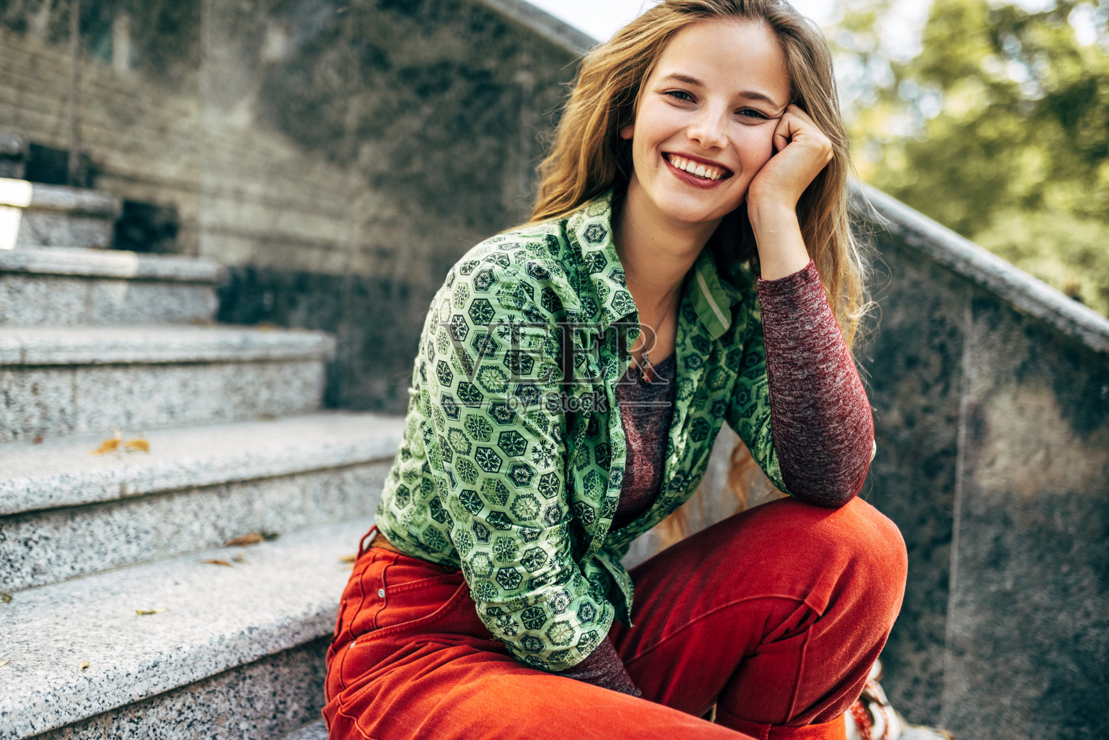 户外的形象，一个快乐的年轻女学生微笑着健康的微笑看镜头，坐在旁边的大学校园在一个阳光明媚的日子。美女在外面的街道上休息。照片摄影图片