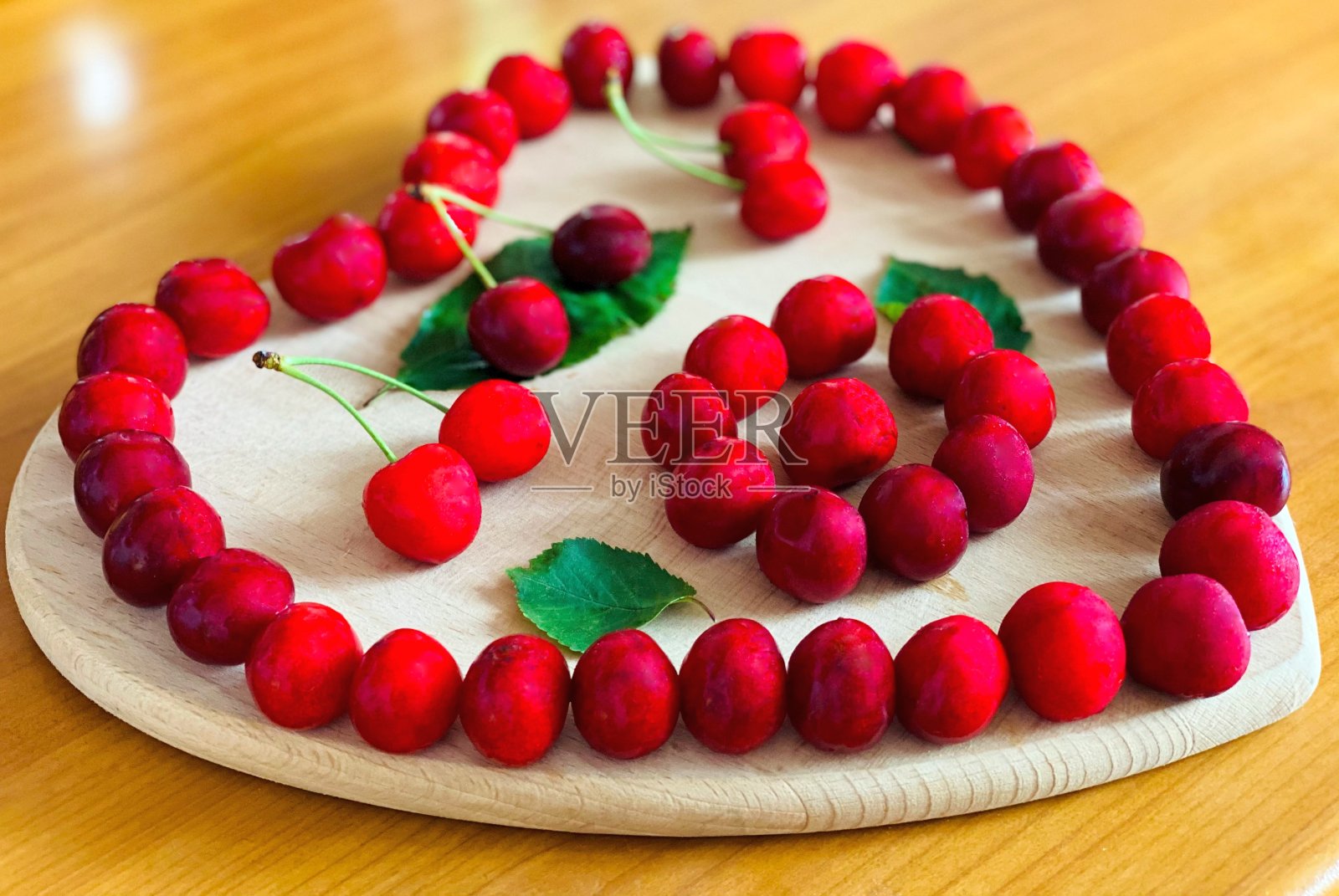 红色的甜樱桃浆果放在心形的木板上。照片摄影图片
