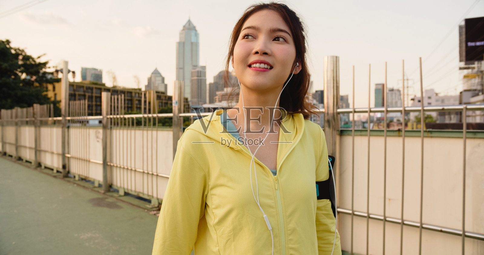 美丽年轻的亚洲女运动员练习使用智能手机听音乐，同时在城市环境中跑步。照片摄影图片