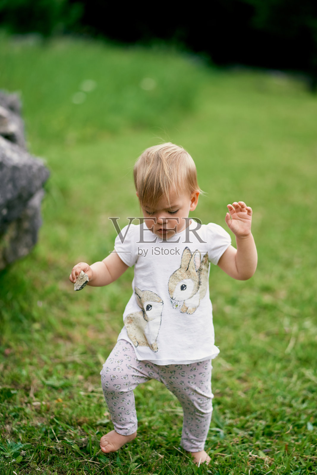 手里拿着一颗鹅卵石的孩子走过一片绿色的草地照片摄影图片