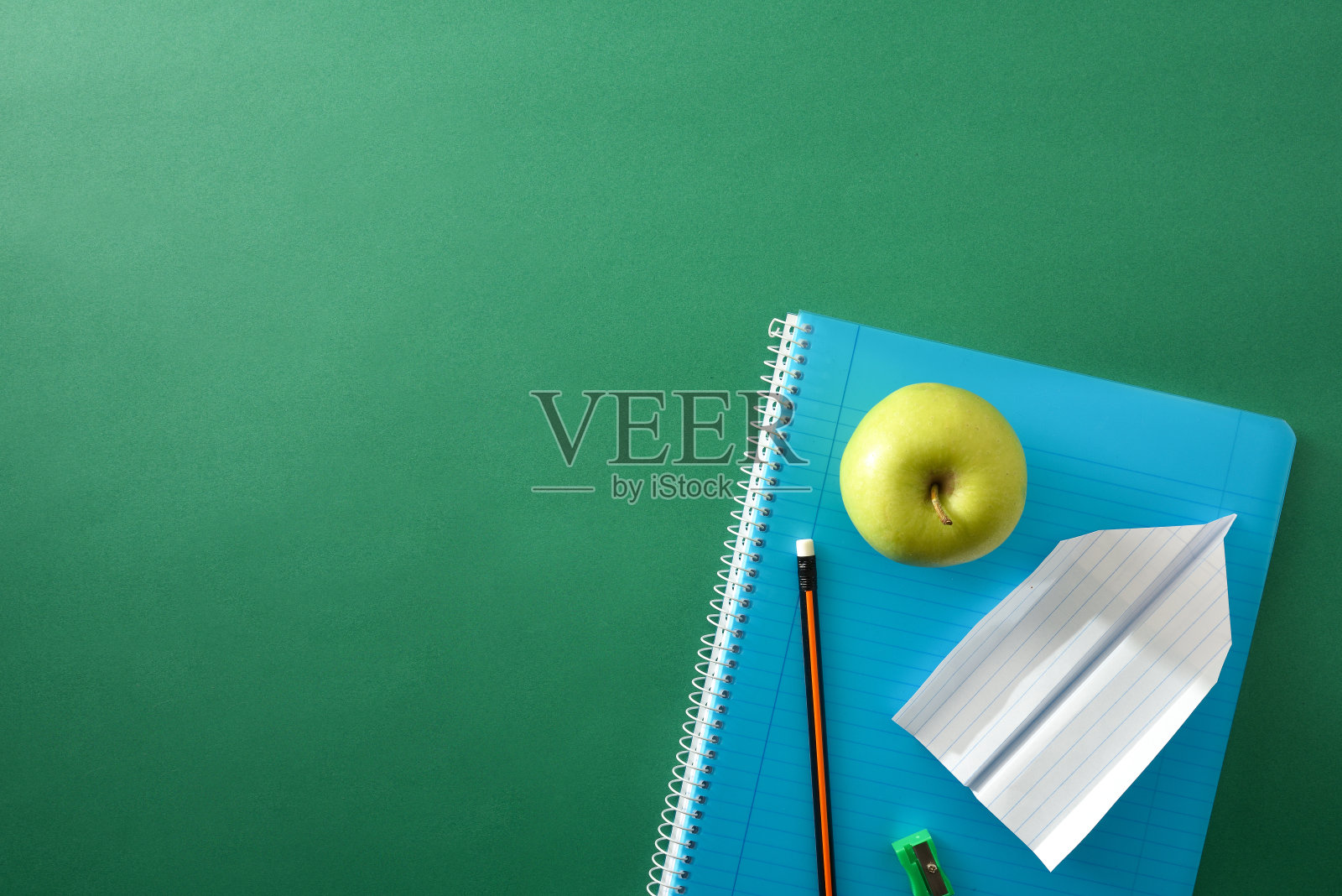带铅笔和卷笔刀的蓝色螺旋笔记本，绿色背景照片摄影图片