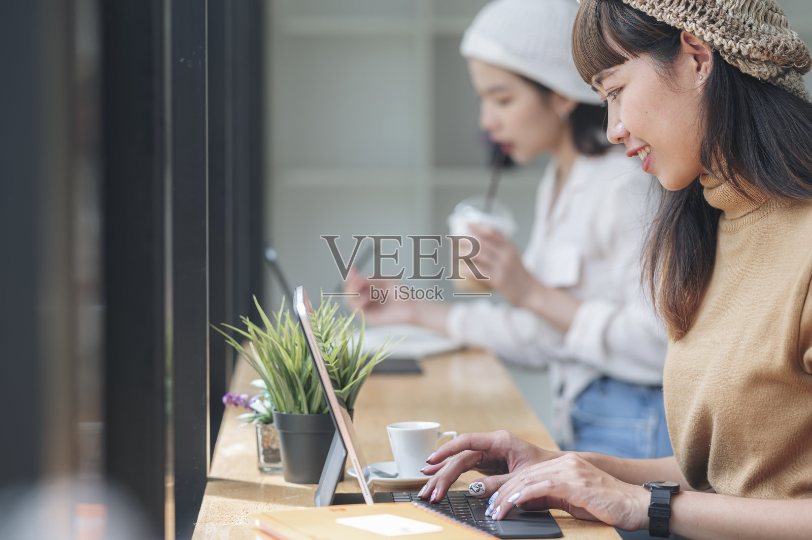 年轻的亚洲女性在共同工作空间愉快地使用平板电脑的侧面视图。照片摄影图片