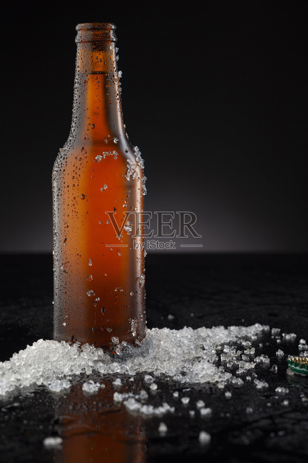 冰冷的棕色啤酒瓶上覆盖着冰和水滴-凝结。空白饮料饮料产品设计模型。站在黑色的桌子上，黑色的背景。照片摄影图片