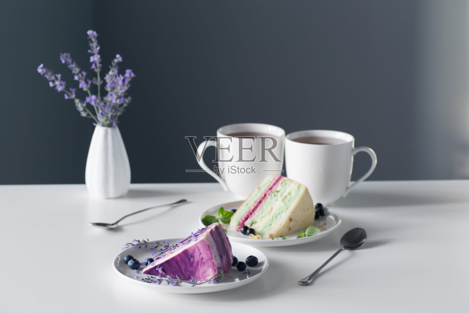 背景是灰色的墙壁，白色的桌子上放着浆果芝士蛋糕和两杯茶照片摄影图片