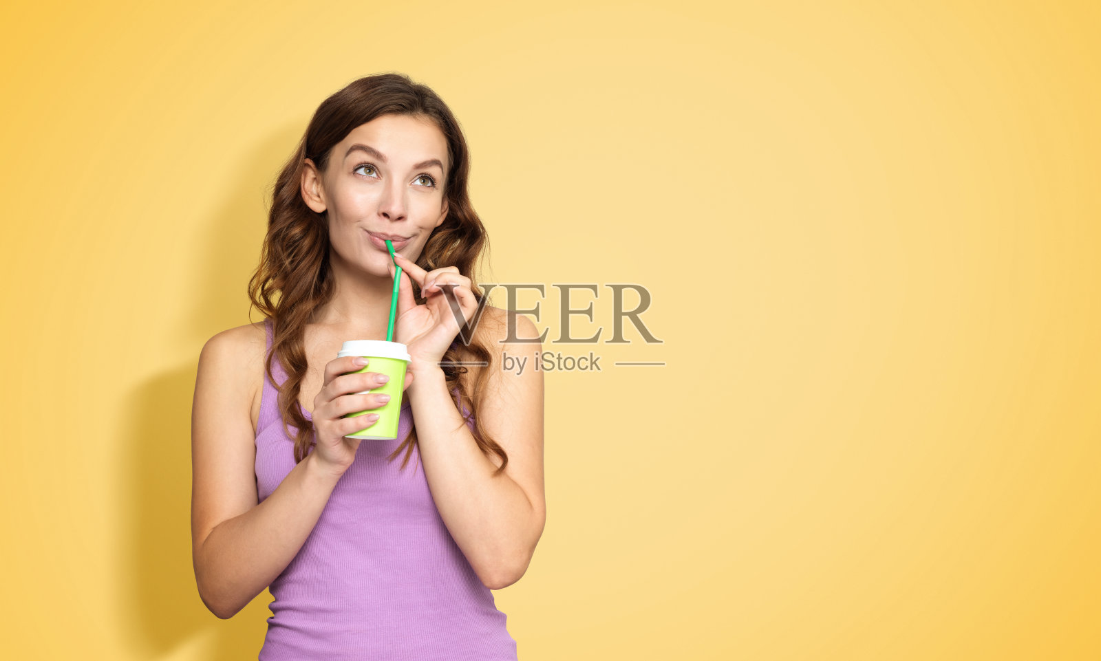 一个快乐的小女孩用吸管喝着纸杯里的水，看着远处黄色的背景照片摄影图片