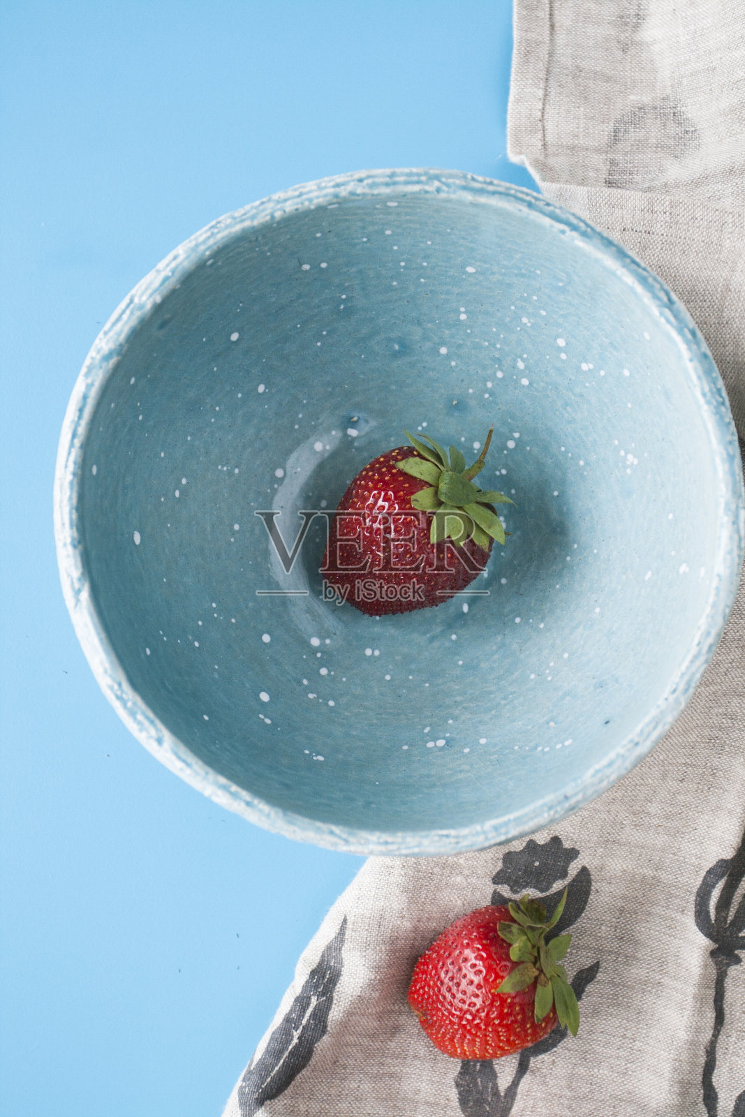 一个红色多汁的草莓放在蓝色的深盘子里，背景是蓝色的。接下来是亚麻布湿巾。前视图。照片摄影图片