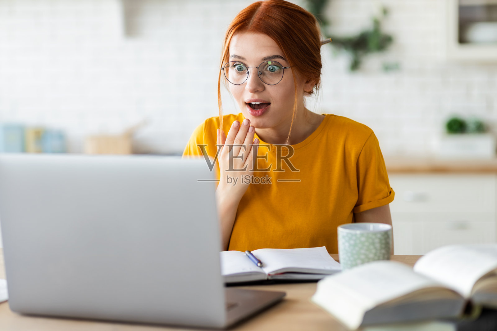 红发年轻女孩坐在桌边拿着笔记本电脑意外收到电子邮件，激动不已照片摄影图片