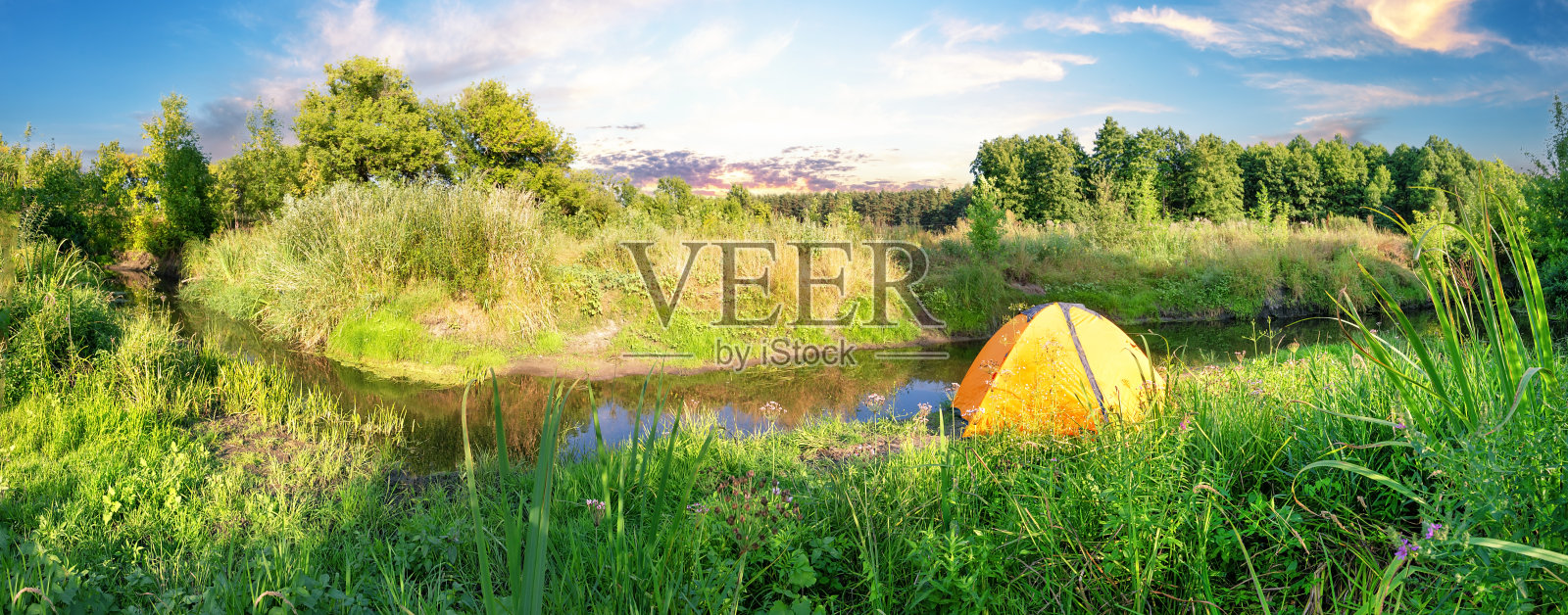 橘黄色的帐篷在河岸上覆盖着郁郁葱葱的绿草照片摄影图片