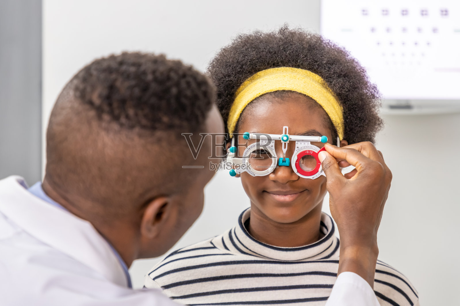 非洲年轻的女孩在诊所或眼镜店用试用框架与男性验光师做眼睛检查。护眼的概念。照片摄影图片