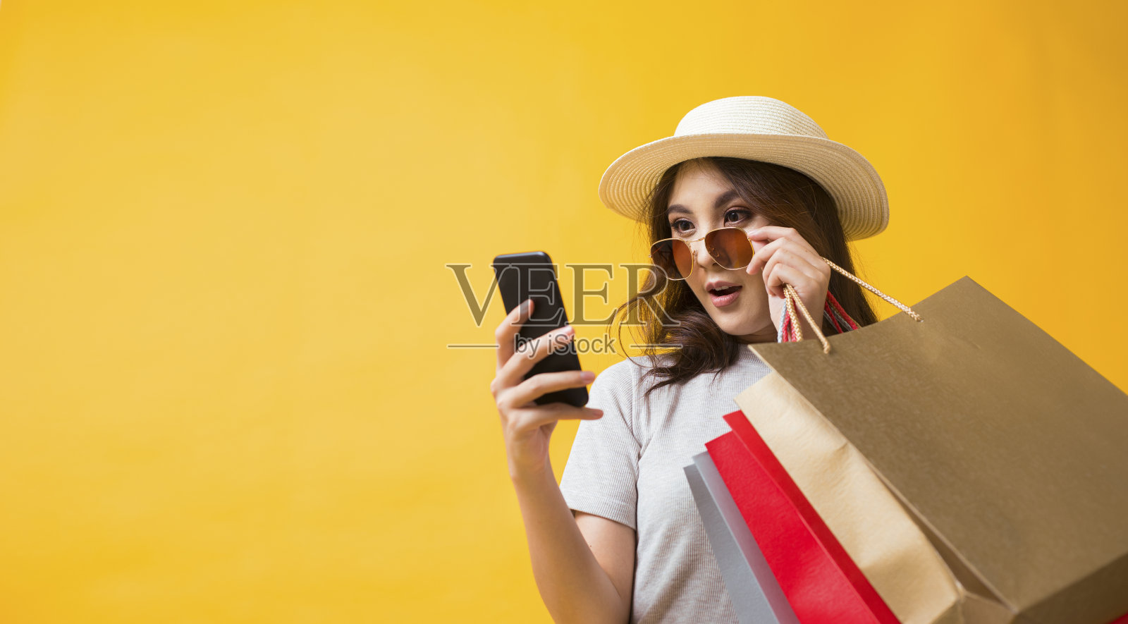 黄色背景下，微笑的亚洲女性用智能手机和信用卡在网上购物。照片摄影图片