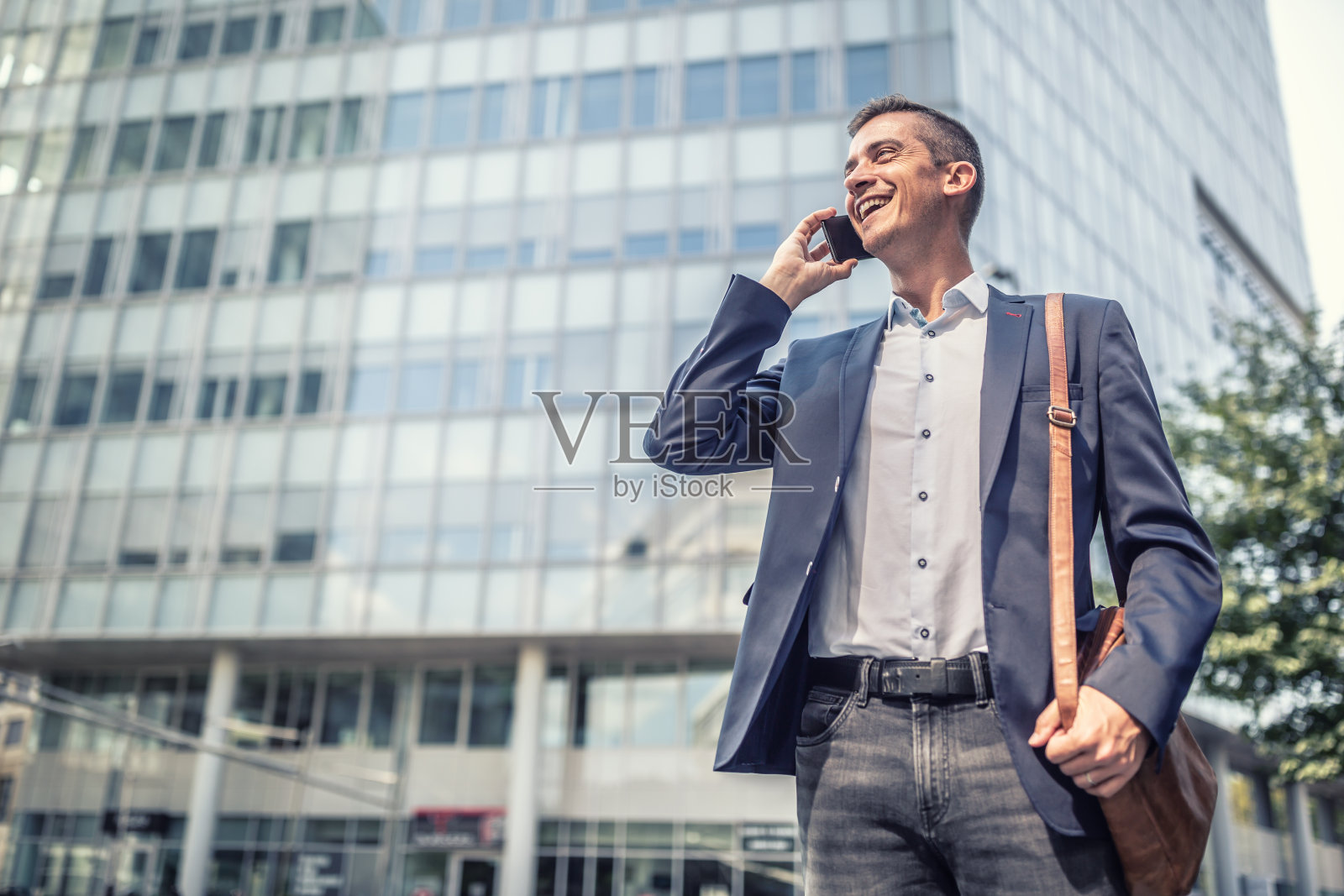 在办公大楼前微笑着打电话的男士穿着商务休闲装。照片摄影图片