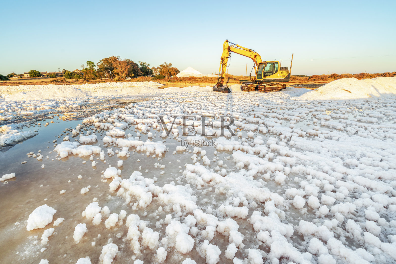 在葡萄牙法罗的盐碱地，用黄色挖掘机收获海盐照片摄影图片