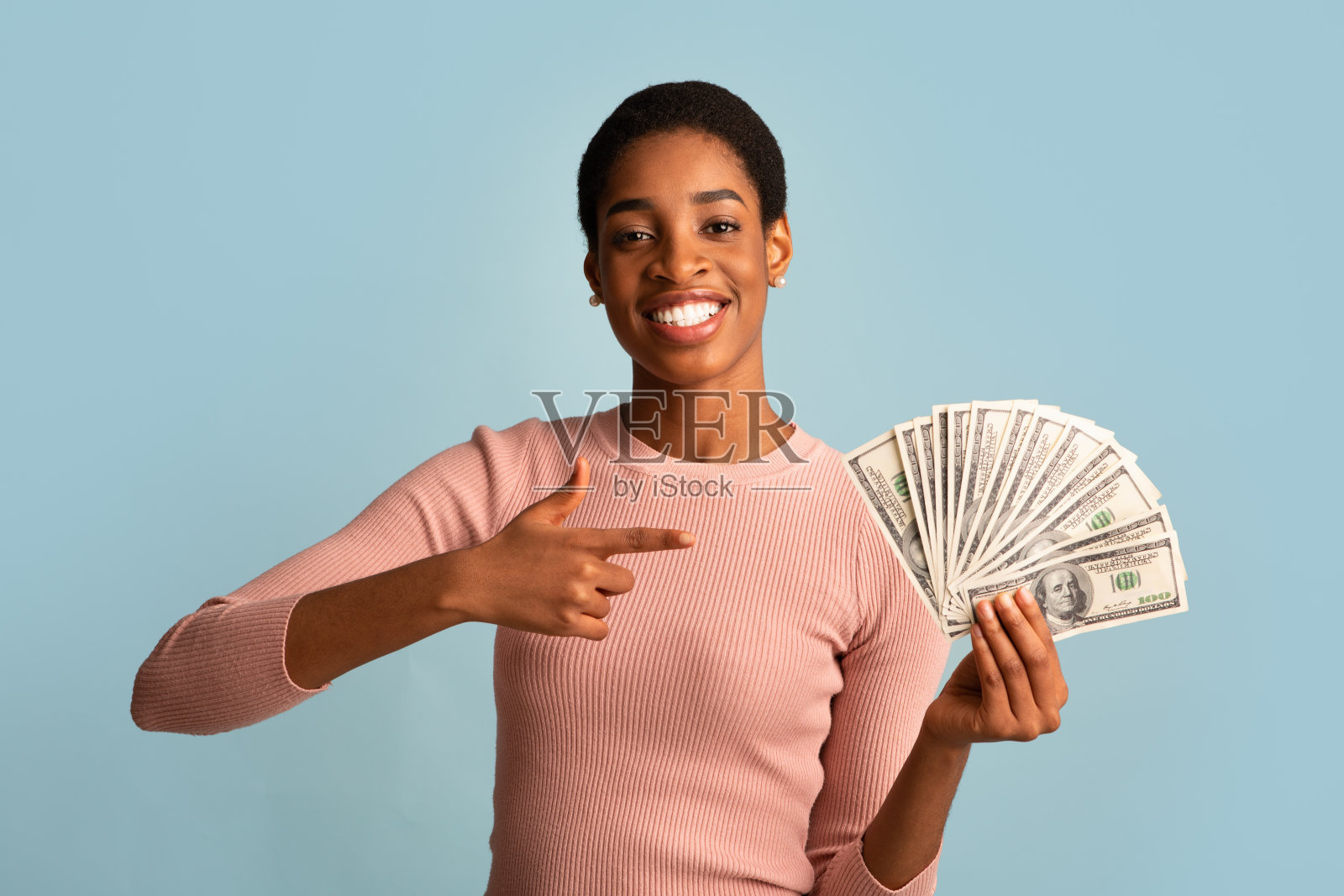 欢快的年轻非洲裔美国妇女指着她手臂里的美元现金照片摄影图片