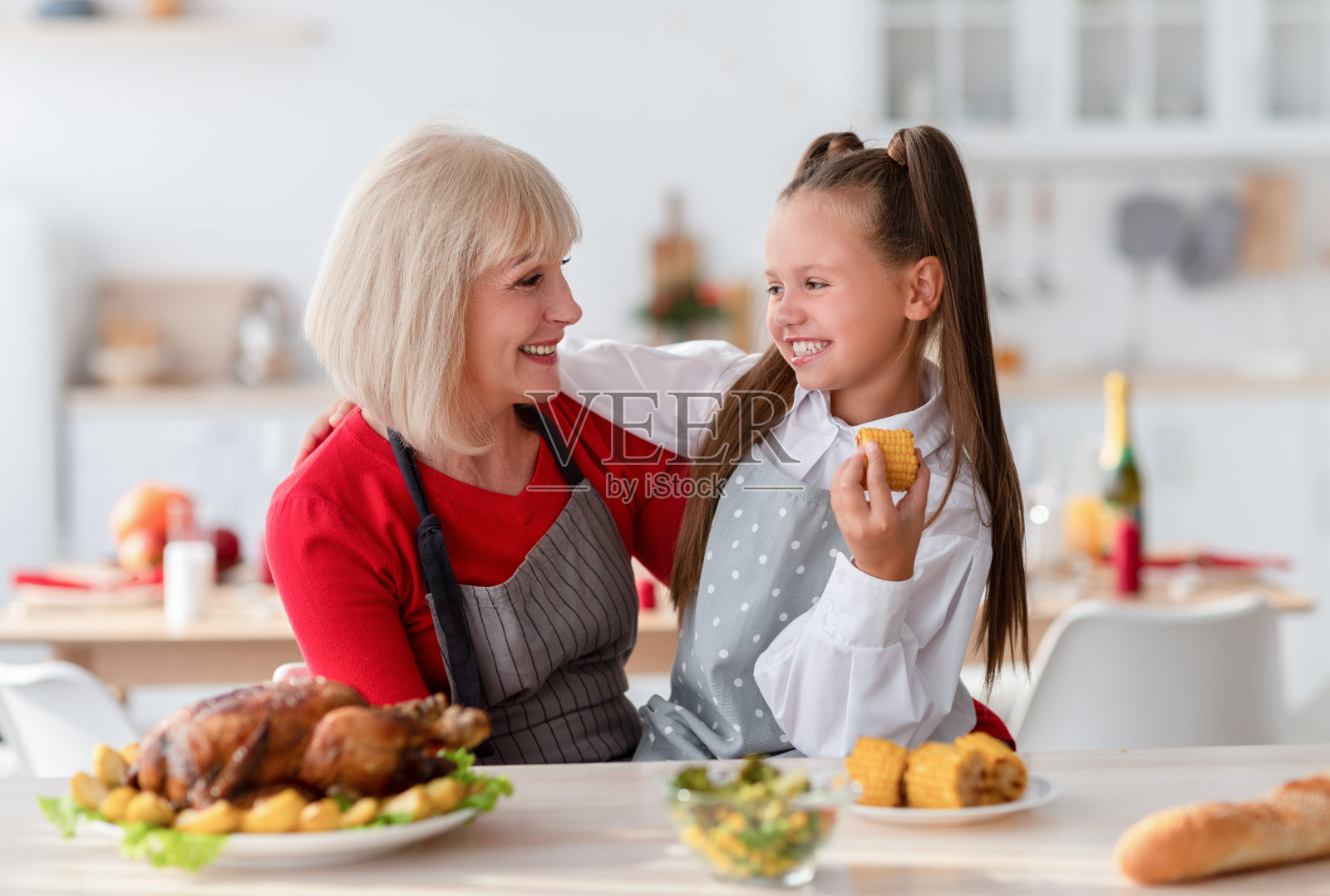 家庭烹饪。快乐的奶奶抱着可爱的女孩，在厨房做传统的感恩节或圣诞节晚餐照片摄影图片