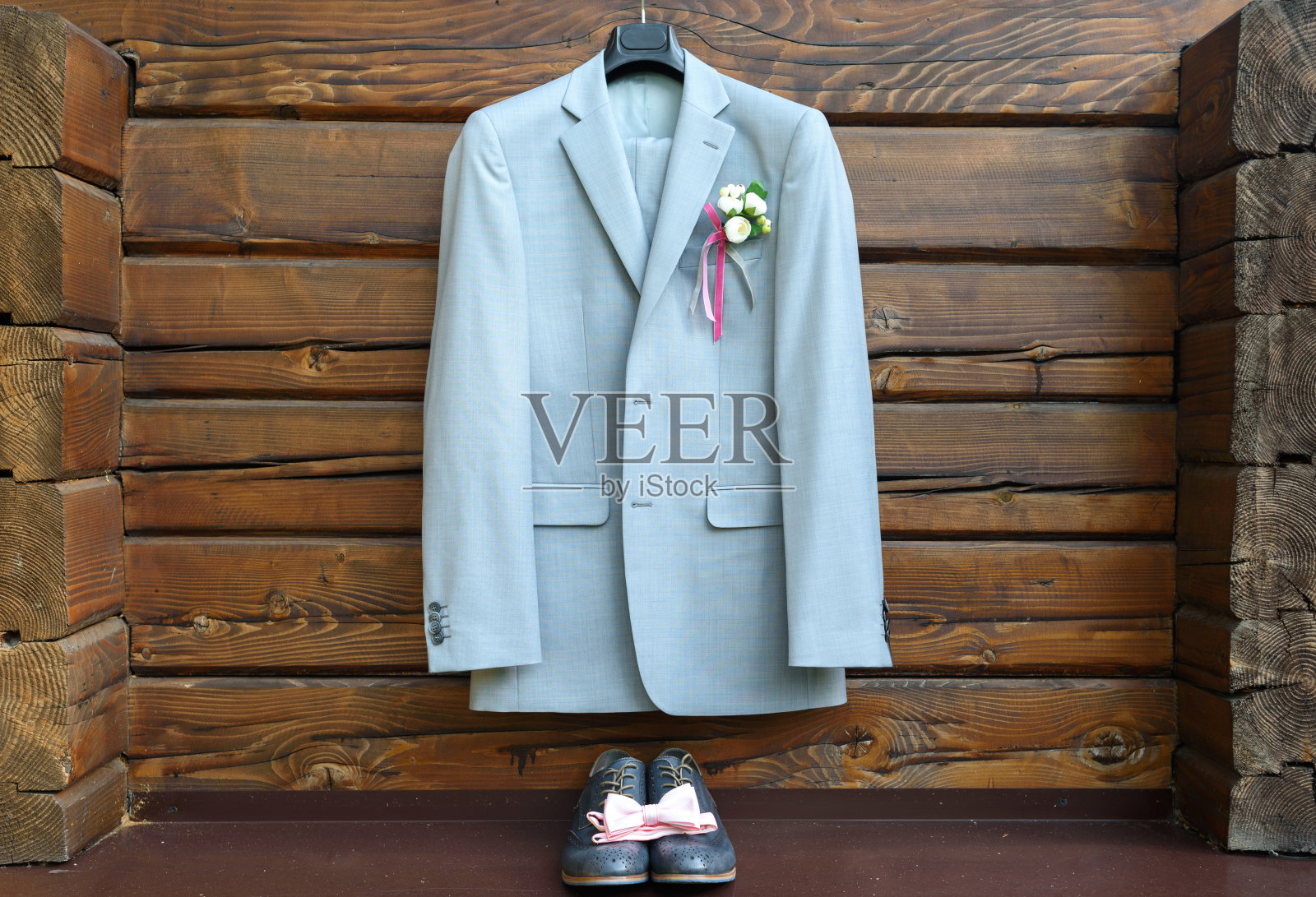 风格优雅的婚礼新郎套装，木制背景上挂着纽扣孔。灰色西装挂在皮革新郎鞋和粉红色领结上面。新郎婚礼饰品，自由空间照片摄影图片